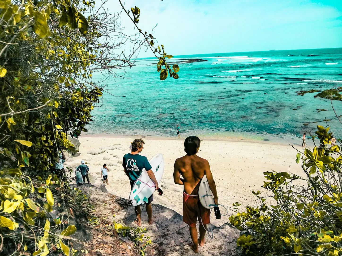 Surfers walking down to a turquoise beach.